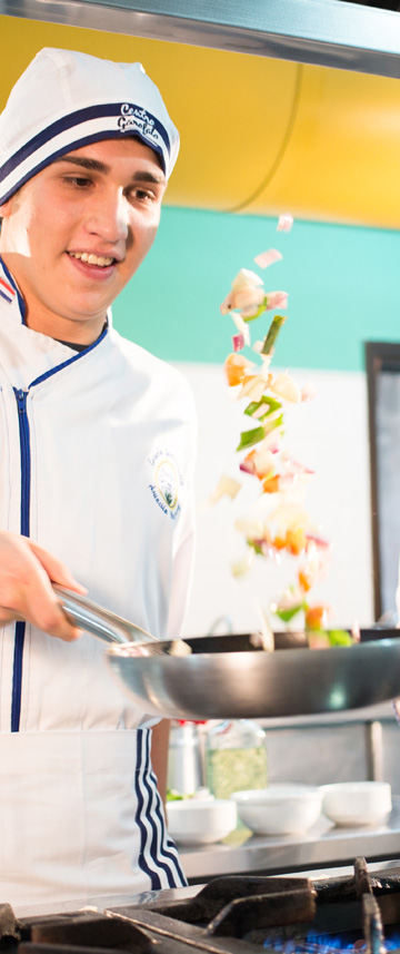 Alumno saltea verduras al fuego en la cocina taller.